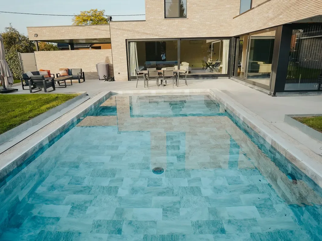 Piscine à fond de dalles bleu-vert vue de près, reflets de la façade en briques de la maison