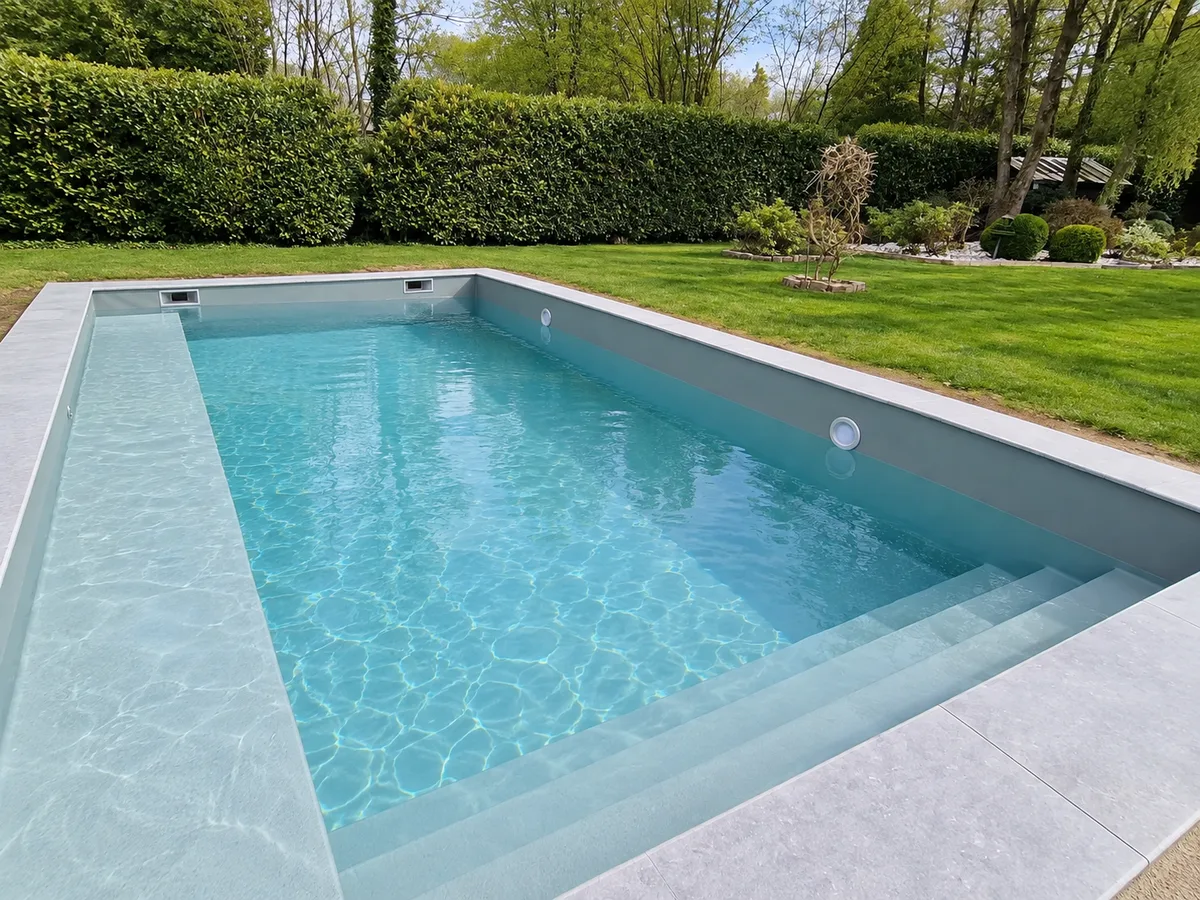 Piscine rectangulaire gris clair, eau turquoise, large escalier immergé, margelles grises et jardin aux haies taillées