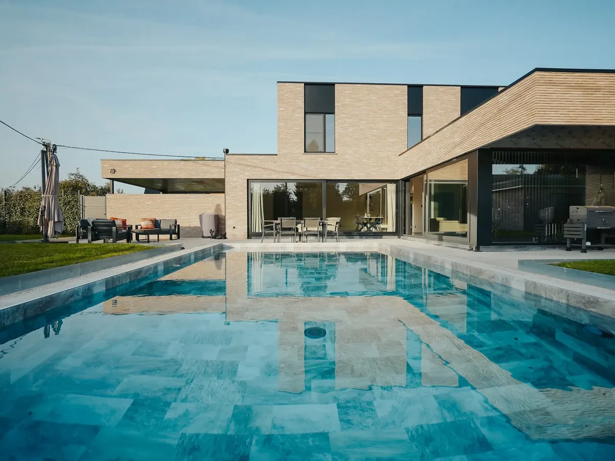 Piscine rectangulaire à l'eau claire dont la surface reflète la façade en briques de la maison, terrasse au fond